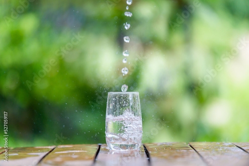 Water falls on a glass that is placed on a wooden stick with water splashing.