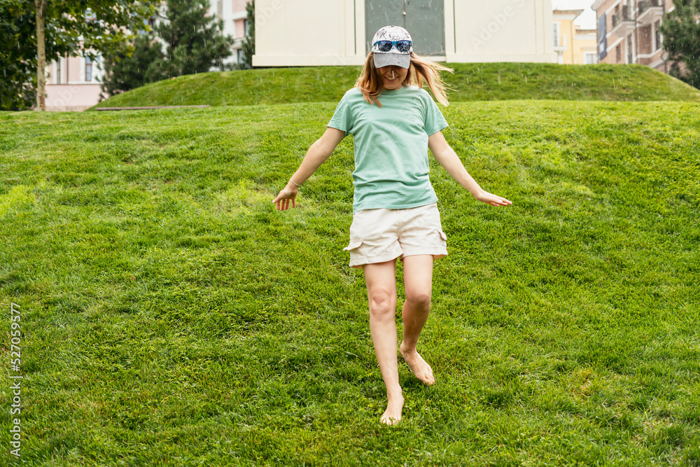 happy young woman barefoot walking on green grass lawn enjoying the warm rain in Summer enjoying nature feeling