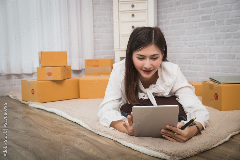 Business woman accepts orders from customer via online sales while lying on carpet in her home office, prepare parcel box of product for deliver to customer. Business woman accepts orders from customer via online sales while lying on carpet in her home office, prepare parcel box of product for deliver to customer.
