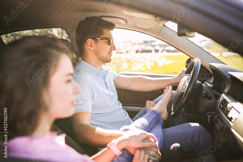 A young man holding his girlfriend’s hand in a car and driving  © racool_studio