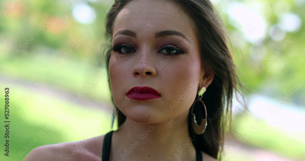 Portrait of young hispanic woman face looking to camera. Serious girl staring in outdoors Portrait of young hispanic woman face looking to camera. Serious girl staring in outdoors