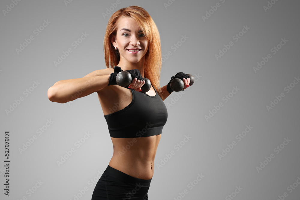 Naklejka premium Sporty, muscular female fitness trainer in sportswear posing with dumbbells on a dark background.
