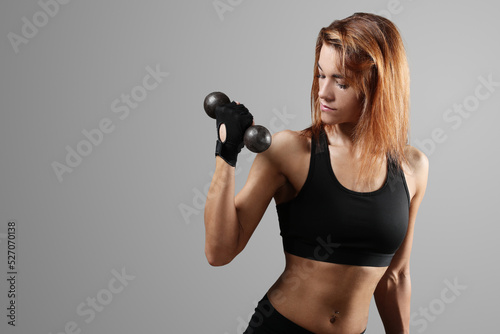 A sporty, muscular woman in sportswear doing exercises with dumbbells on a dark background. © racool_studio