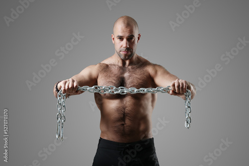 Young strong sporty toned bodybuilder training with metal chain