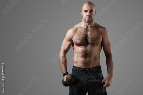 Sporty muscular bodybuilder posing with dumbbells on a dark background