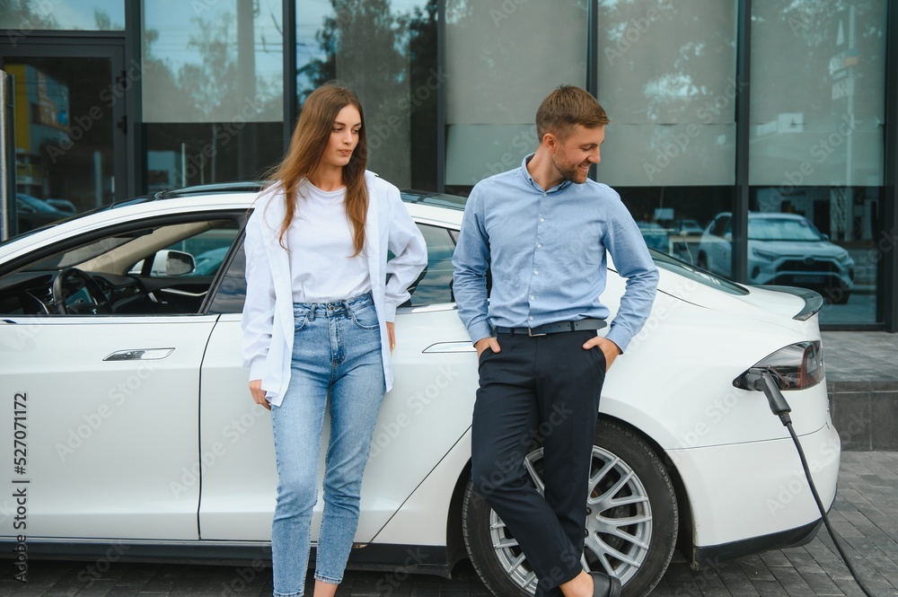 Smiling man and woman on the charging station for electric cars. A man is charging a car. Smiling man and woman on the charging station for electric cars. A man is charging a car.