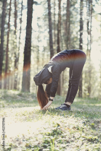 Photo of a young beautiful brunette woman doing stretches early in the morning in nature
