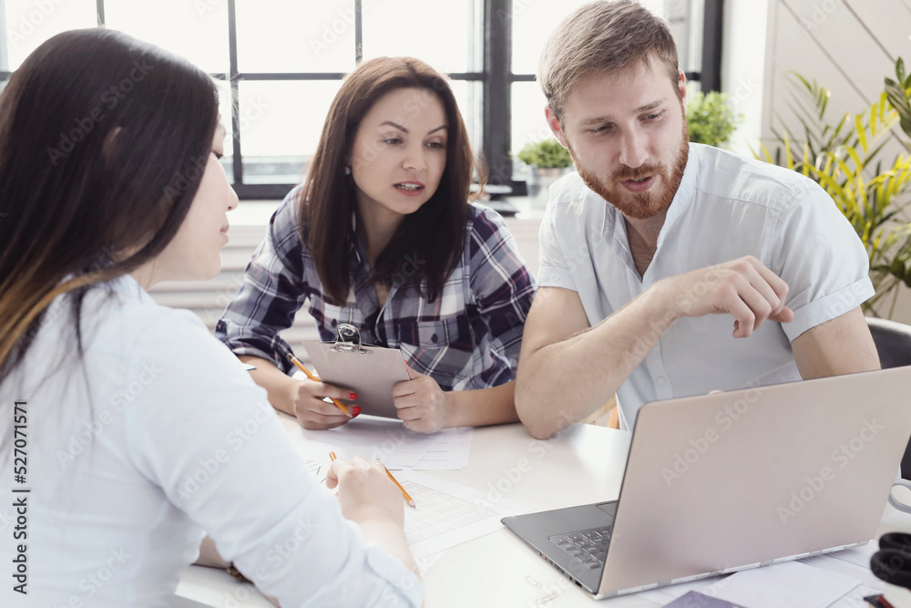 Three young partners discuss business plan using computer at office 
