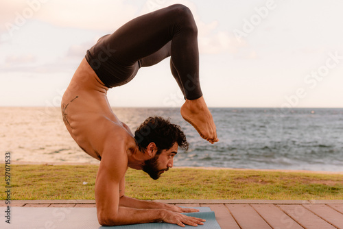 Young beautiful man practicing ashtanga yoga at sunset on the beach. Doing exercises and stretching. Scorpion Pose