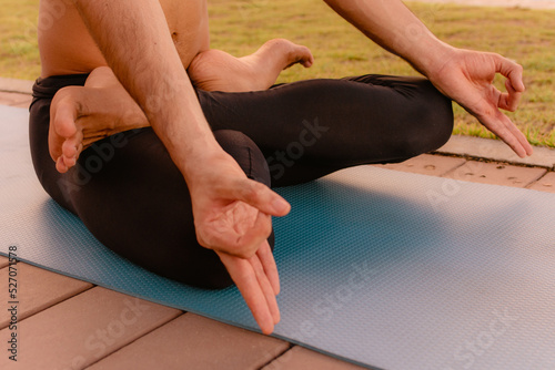 Young beautiful man practicing ashtanga yoga at sunset on the beach. Doing exercises and stretching. Net-Bearer Bond Pose