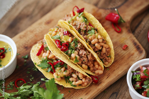 Close view of fresh Mexican tacos with meat and vegetable fillings on a wooden cutting board