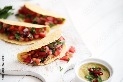 Traditional fresh Mexican tacos with sliced tomatoes and greens on a white cutting board