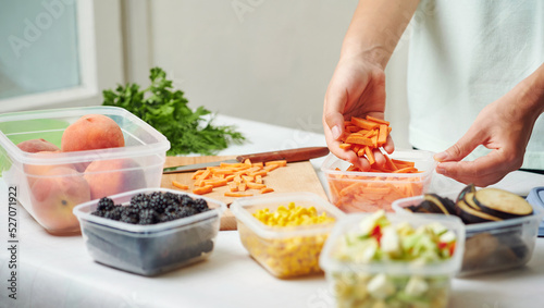 Fotografie Woman holding plastic container with slices of carrot at table in kitchen