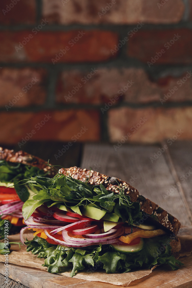 Two fresh, tasty vegetable sandwiches wrapped in paper on a wooden cutting board Two fresh, tasty vegetable sandwiches wrapped in paper on a wooden cutting board