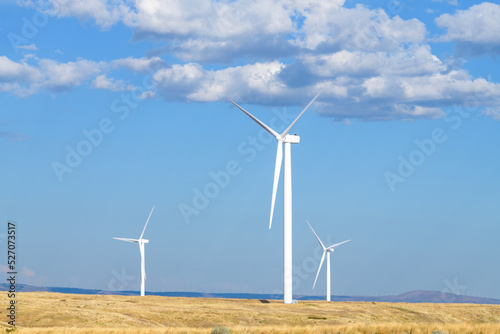 Wind turbines on an arrid hillside in Washington State under a blue sky with yellow grass