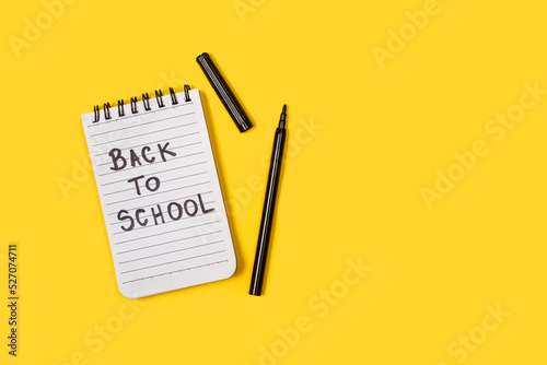 Bloc con la palabra escrita back to school junto a un boli negr sobre un fondo amarllo liso y aislado. Vista superior y de cerca. Copy space photo