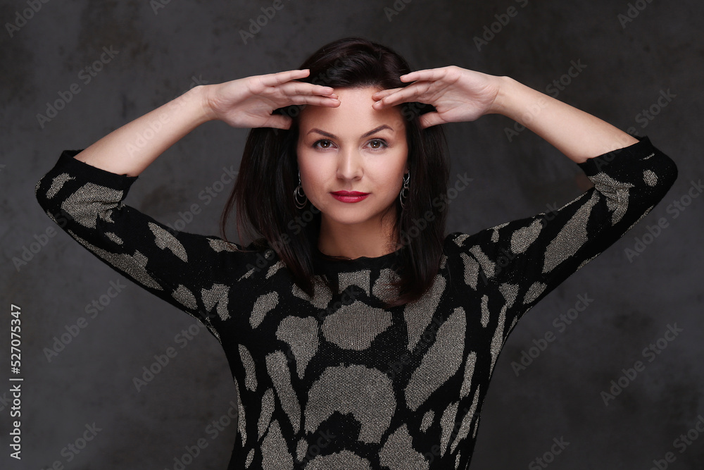 Close-up of an attractive middle aged woman posing with hands on forehead isolated on a dark background.