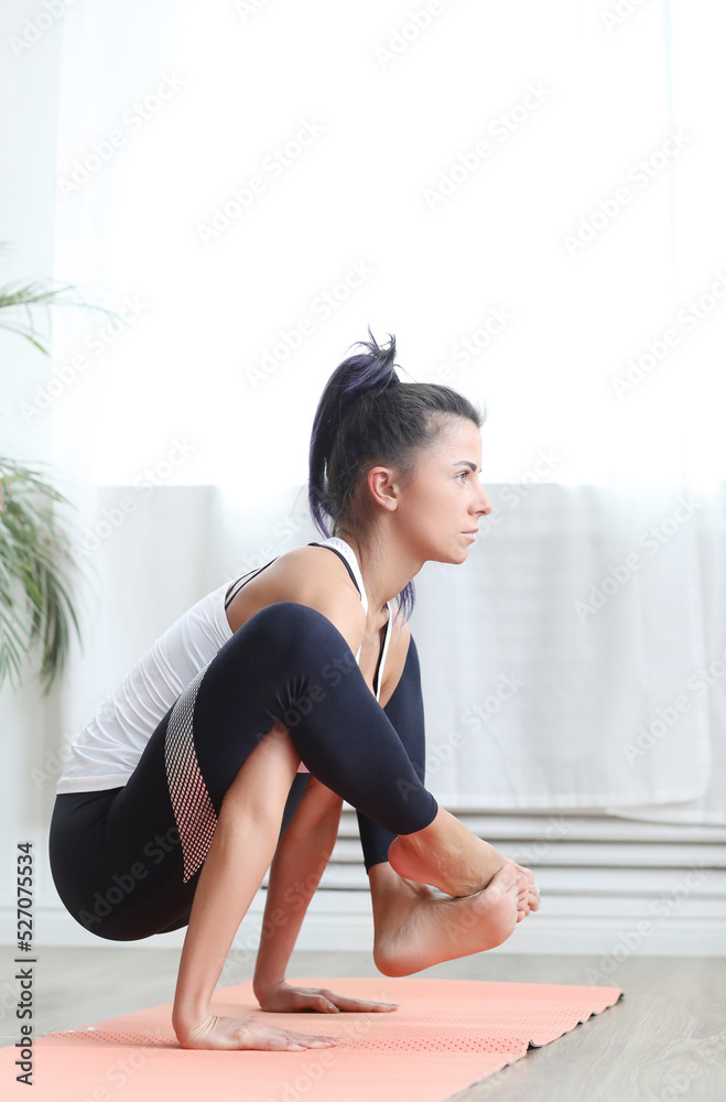 Beautiful female fitness trainer doing yoga exercises, arm balance exercise with crossed legs on yoga mat