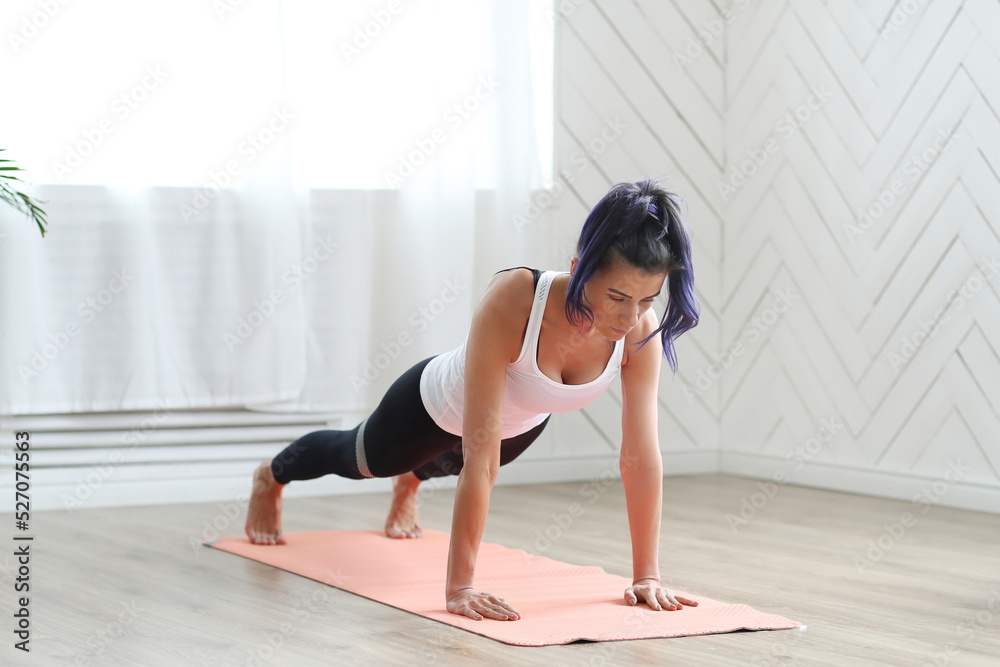 A full-size portrait of an attractive young woman doing home yoga or pilates exercises on a rug, standing in a board position (phalankasana) A full-size portrait of an attractive young woman doing home yoga or pilates exercises on a rug, standing in a board position (phalankasana)