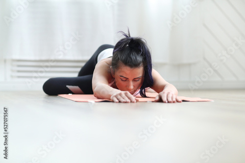 A portrait of an attractive, young woman doing home yoga or pilates exercises on a rug, standing in a child pose