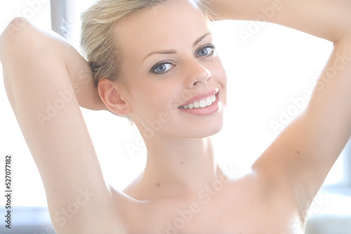 Close-up photo of a young, beautiful, naked girl with hands behind her head