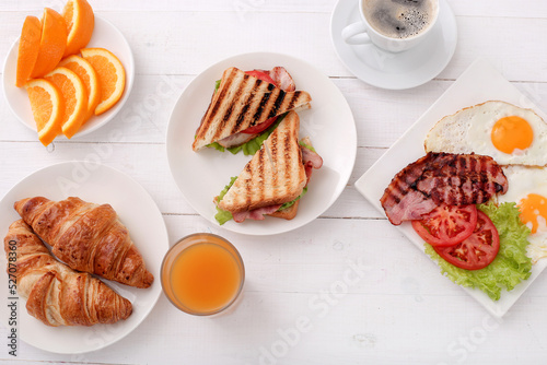 Top view of morning breakfast with fried eggs,bacon,sliced vegetables,croissants and a cup of coffee on a wooden background