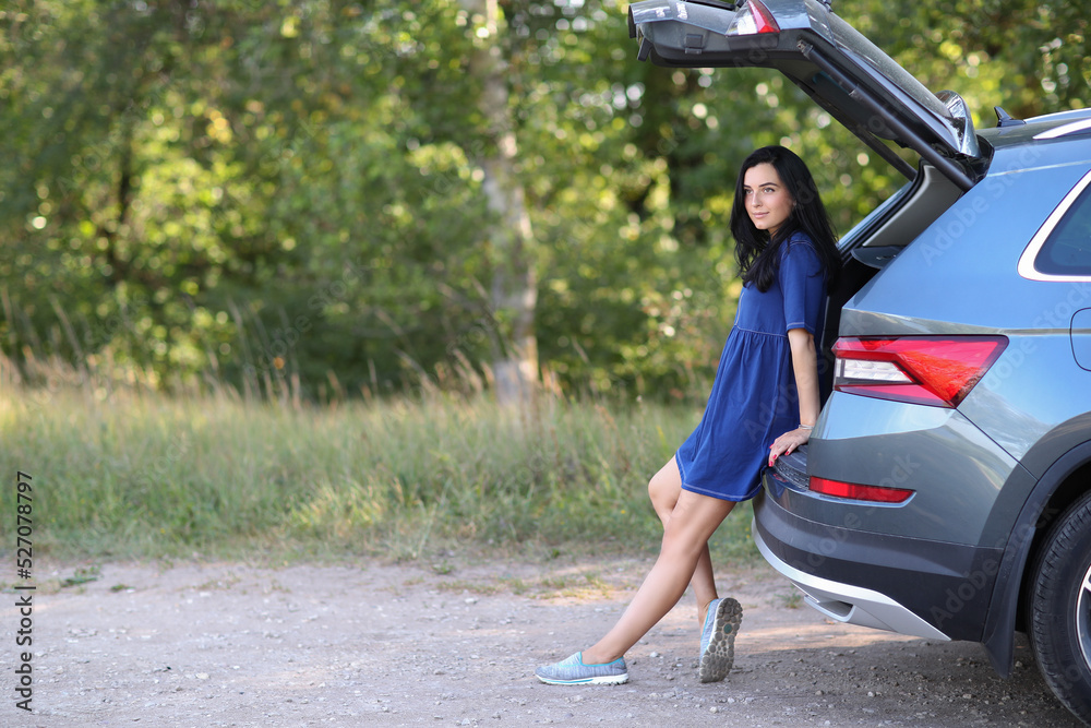 Portrait of a young woman with blue dress sitting at car trunk Portrait of a young woman with blue dress sitting at car trunk