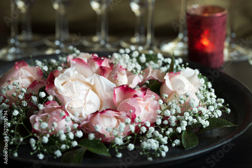 Schöne Rosen als Dekoration zur Hochzeit mit Schleierkraut auf rundem Tablett vor Gläsern und rotem Kerzenlicht 