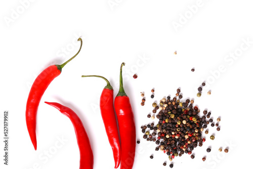 Black, red, white, and green peppercorns with four red hot chili peppers on a white background. 