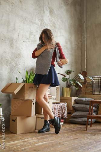 Full size photo of a cute girl in black skirt trying new gray sweater on the background of cardboard boxes