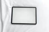 Top view tablet with blank desktop white screen white bed at home, crumpled beige blanket, Overhead shot 