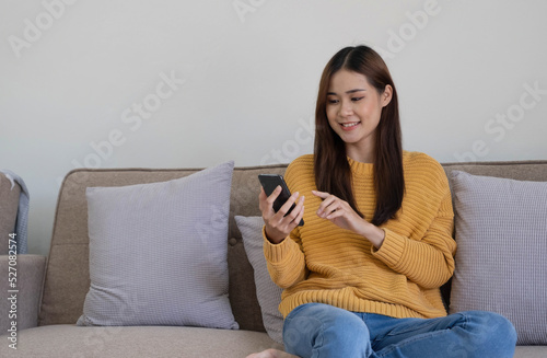 Happy asian woman using mobile phone. Smiling young female using app shopping online, ordering delivery relax on sofa at home.