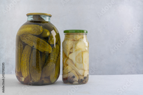Pickled cucumbers in a glass jar on a light background. Homemade fermented or pickled cucumbers.