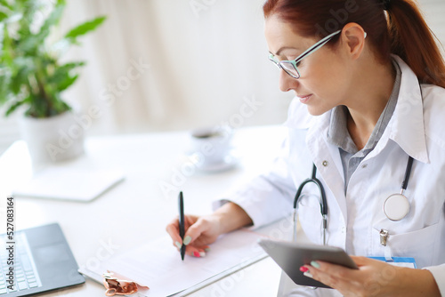 Woman-doctor sitting and working with medication history record forms in hospital or clinic