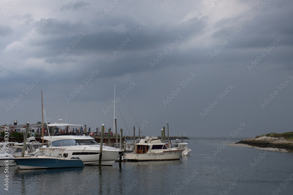Cape Cod coastal scene. Threatening dark gray storm clouds over boats anchored at dock near breakwater entrance to Sesuit Harbor, East Dennis, Massachusetts.