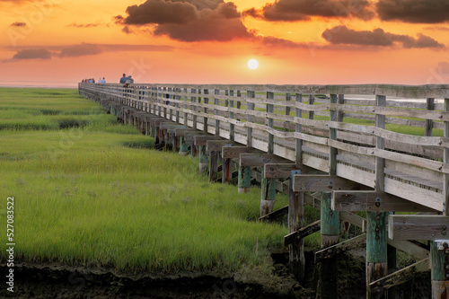 Scenic view of colorful Cape Cod sunset over long raised wooden boardwalk spanning protected saltwater marsh at Grays Beach, Yarmouth Port, Massachusetts.