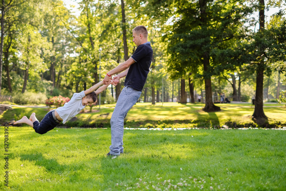 Fototapeta premium Young father twirling his little son in park.