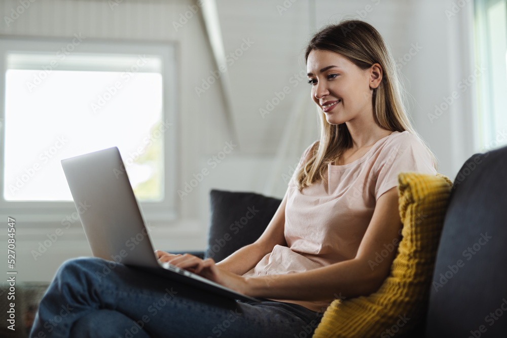 Happy young woman using computer on sofa at home Happy young woman using computer on sofa at home