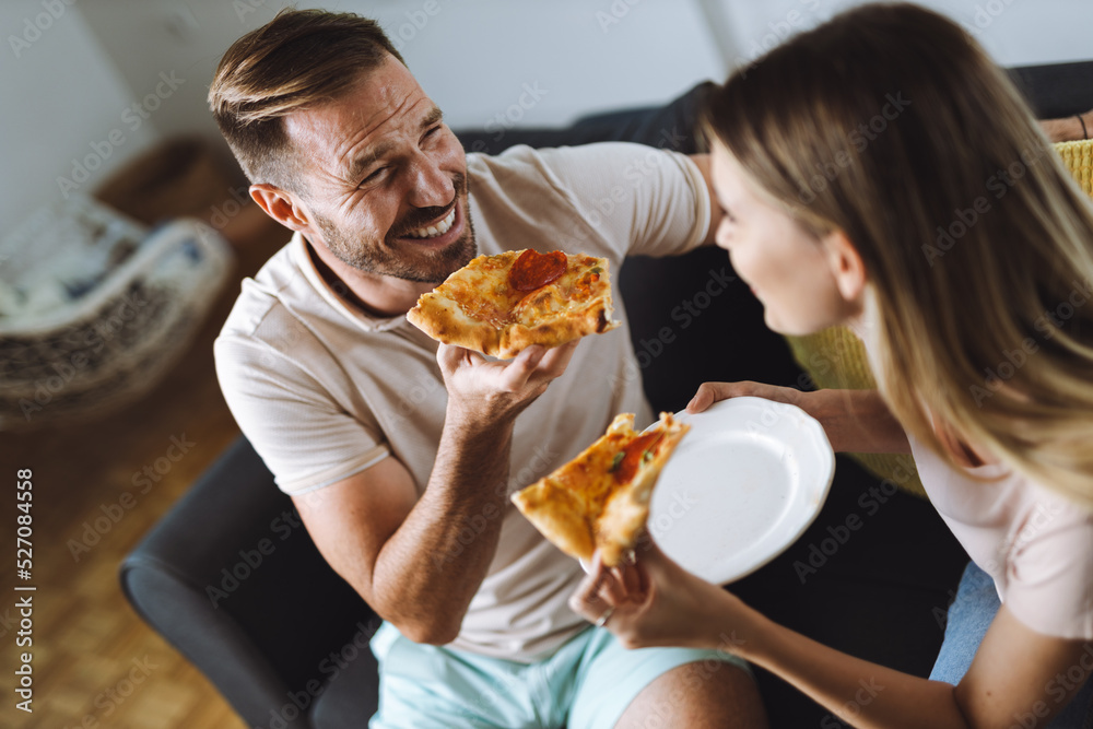 Happy young couple eating pizza for lunch in the living room