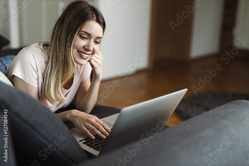 Happy young woman surfing the net while relaxing in the living room