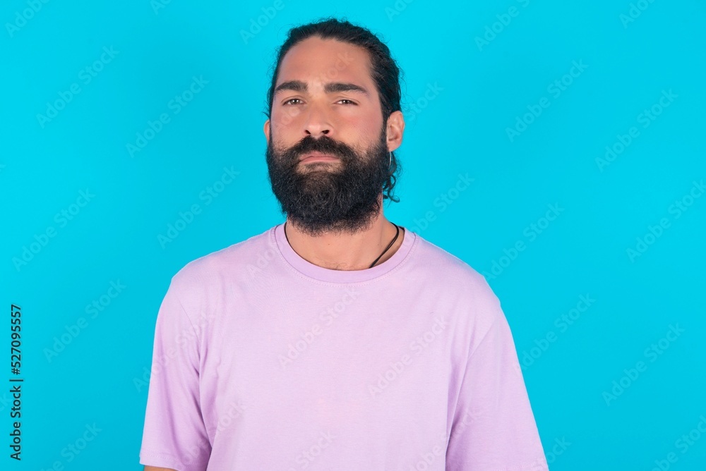 young bearded man wearing violet T-shirt over blue studio background Pointing down with fingers showing advertisement, surprised face and open mouth young bearded man wearing violet T-shirt over blue studio background Pointing down with fingers showing advertisement, surprised face and open mouth