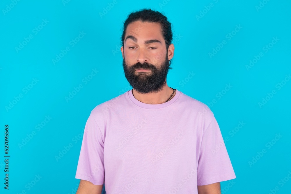 Obraz premium young bearded man wearing violet T-shirt over blue studio background depressed and worry for distress, crying angry and afraid. Sad expression.