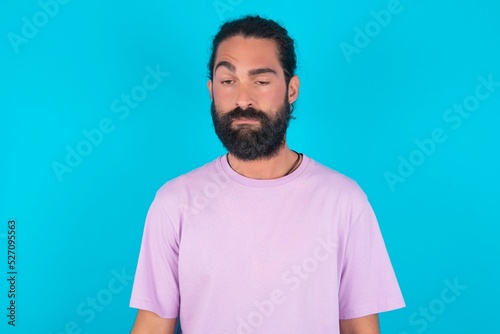 young bearded man wearing violet T-shirt over blue studio background depressed and worry for distress, crying angry and afraid. Sad expression.