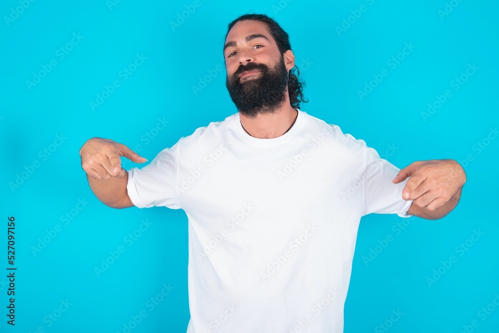 Pick me! Confident, self-assured and charismatic young bearded man wearing white T-shirt over blue studio background promoting oneself as wanting role smiling broadly and pointing at body. Pick me! Confident, self-assured and charismatic young bearded man wearing white T-shirt over blue studio background promoting oneself as wanting role smiling broadly and pointing at body.