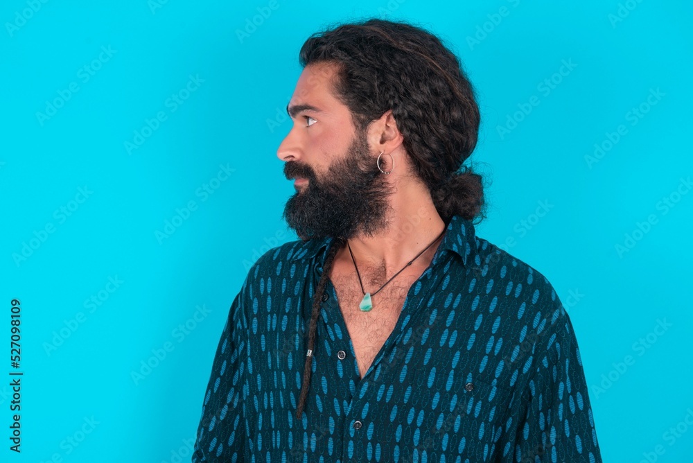 Side view of young happy smiling young bearded man wearing blue shirt over blue studio background Side view of young happy smiling young bearded man wearing blue shirt over blue studio background