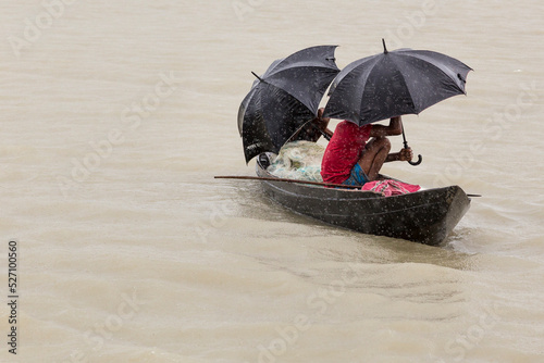 Men in a wooden canoe sheltering under umbrellas from the monsoon rain, Bangladesh