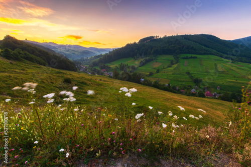 mountainous countryside landscape at dawn. rural fields on the hills. village in the distant valley. gorgeous sky with clouds glowing in morning light