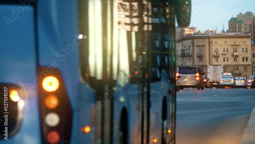 Unknown cars and blue bus drive on along major busy city street in the evening. Mass transit system