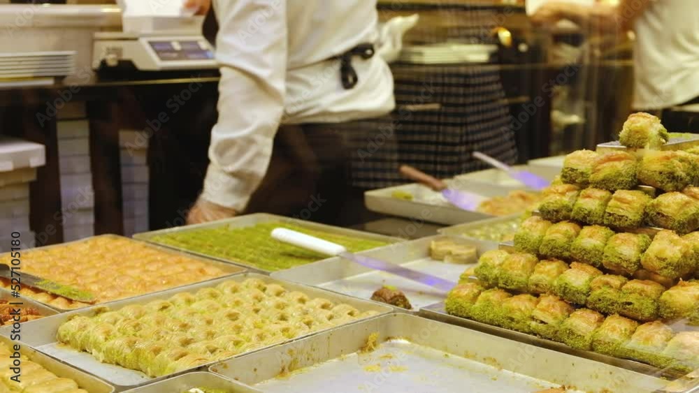 Stacks of baklava at foreground and hands of unrecognizable seller serves customers at traditional turkish delights shop. Showcase of turkish confectionery