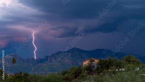 Lightning bolt and monsoon storm clouds over the Catalina Mountains in the Sonoran Desert north of Tucson, Arizona. Beautiful colorful moody sky, windmill, houses and natures furious beauty.